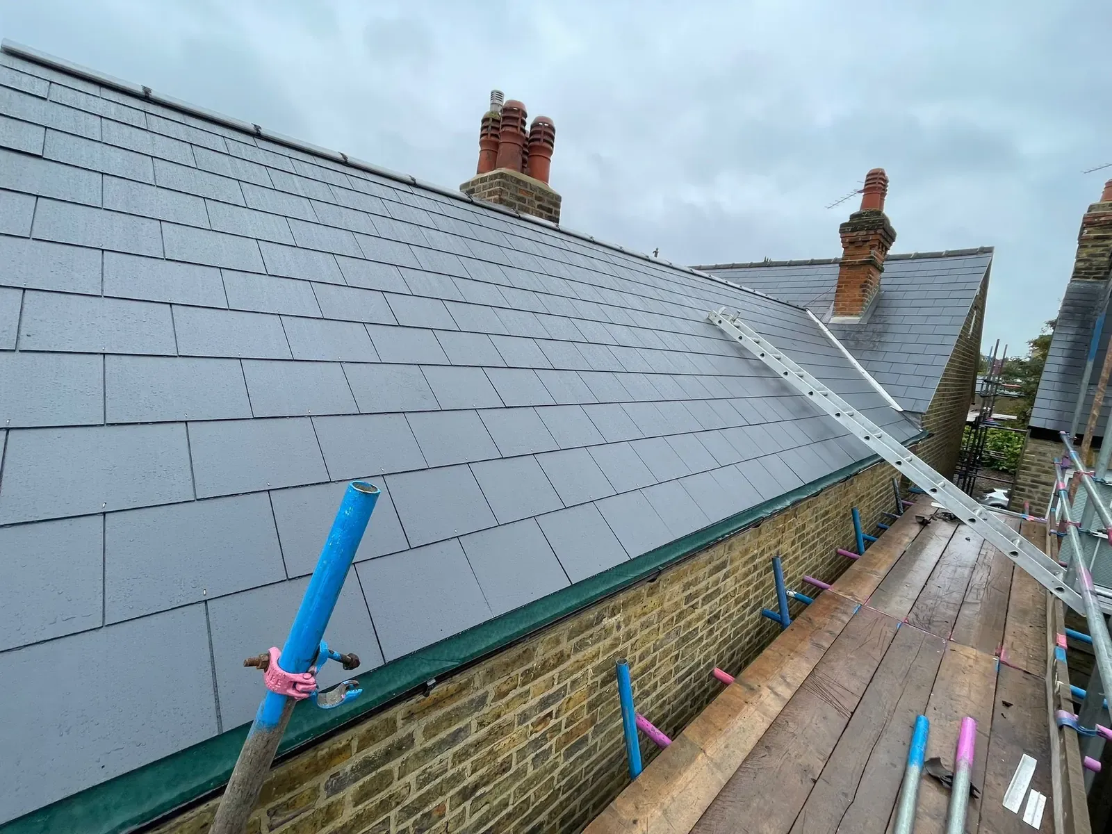 Newly laid slate roof slope with the scaffold walkway along the eaves