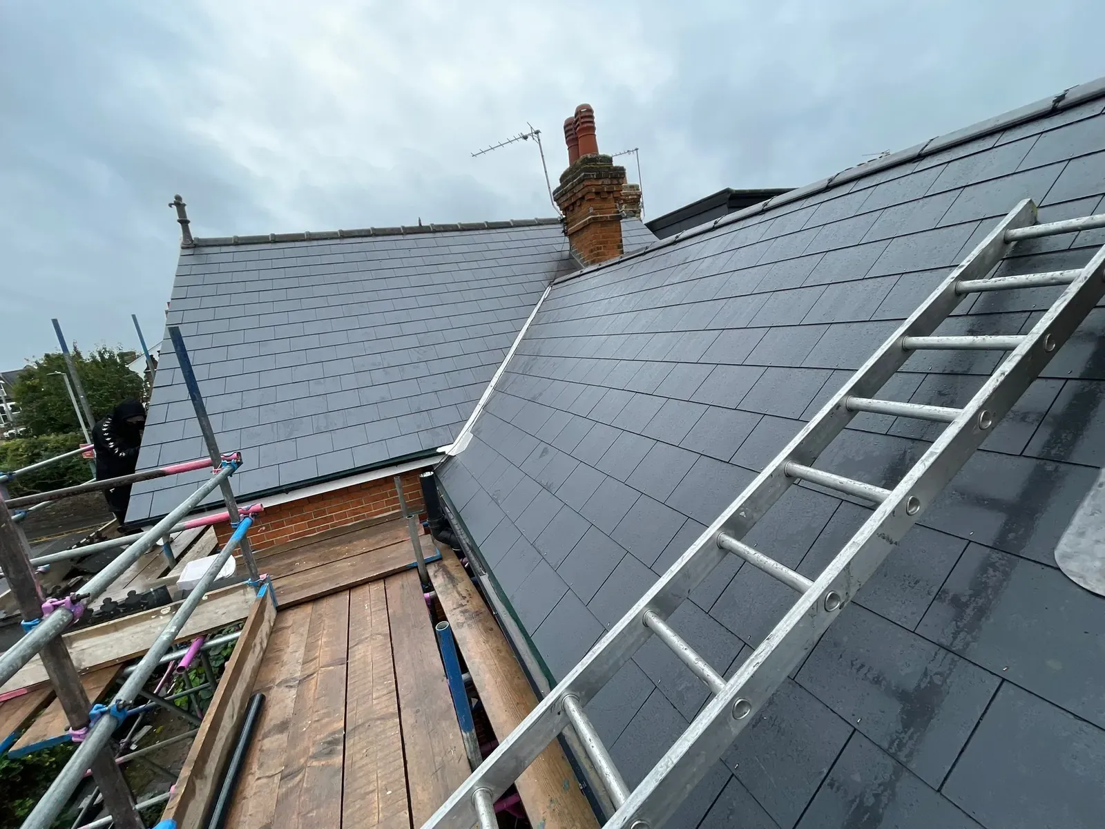Slate re-roof nearly finished, with a ladder on the scaffold and the chimney behind